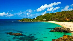 beach with view of shorline and blue ocean during day with blue sky and clouds at Waimea Bay Beach Park in Oahu, Hawaii, USA